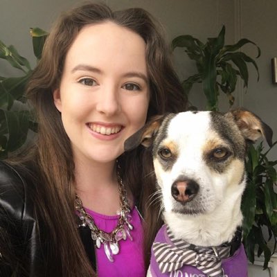 Photo of this week’s host, Brianna, and her Assistance Dog, Kirby. Brianna has long brown hair, pale skin, hazel eyes, and is smiling widely. She is wearing a purple shirt and a black leather jacket. Kirby is a 9kg mix-breed dog sitting on her lap looking towards the camera. He is tri-coloured: mostly white, with patches of brown-black.