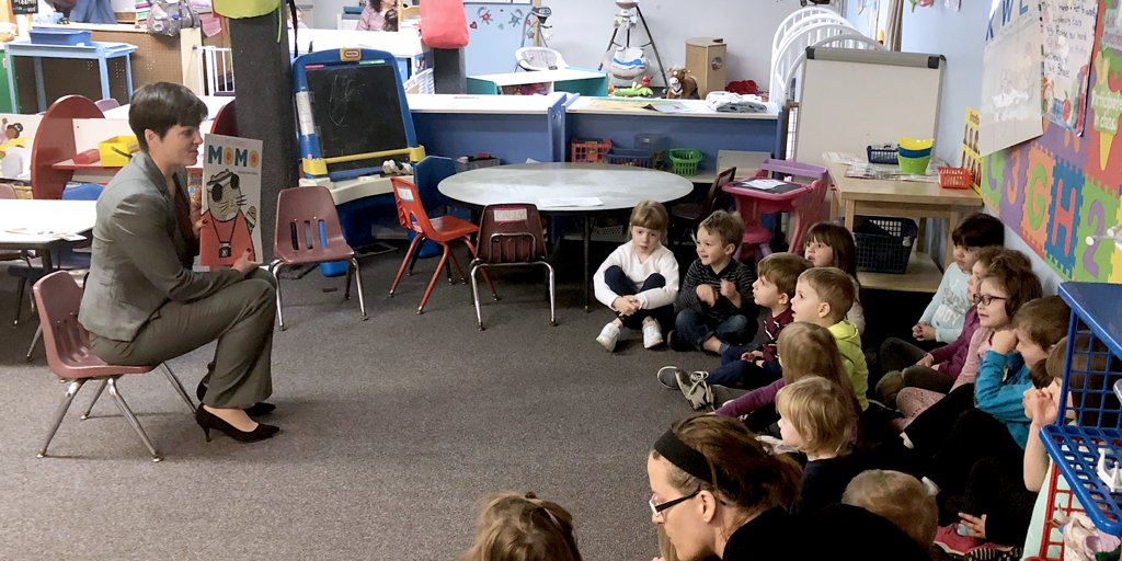 DHS Secretary Teresa Miller reads PA One Book "My Cousin Momo" to a group of children in a colorful classroom.