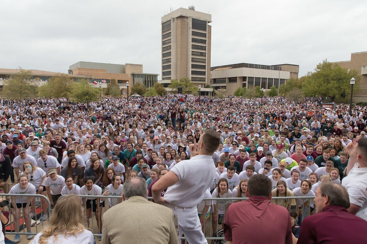 A yell leader leads yells in front of thousands of Aggies in at the Big Event kickoff outside of Kyle Field with Rudder Tower in the background