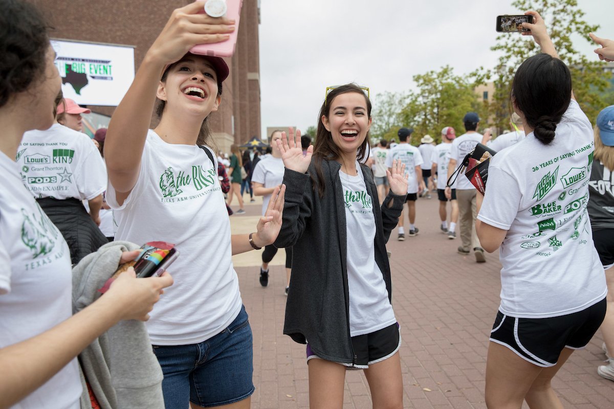 Three girls taking selfies in white Big Event shirts before heading to pickup tools to work