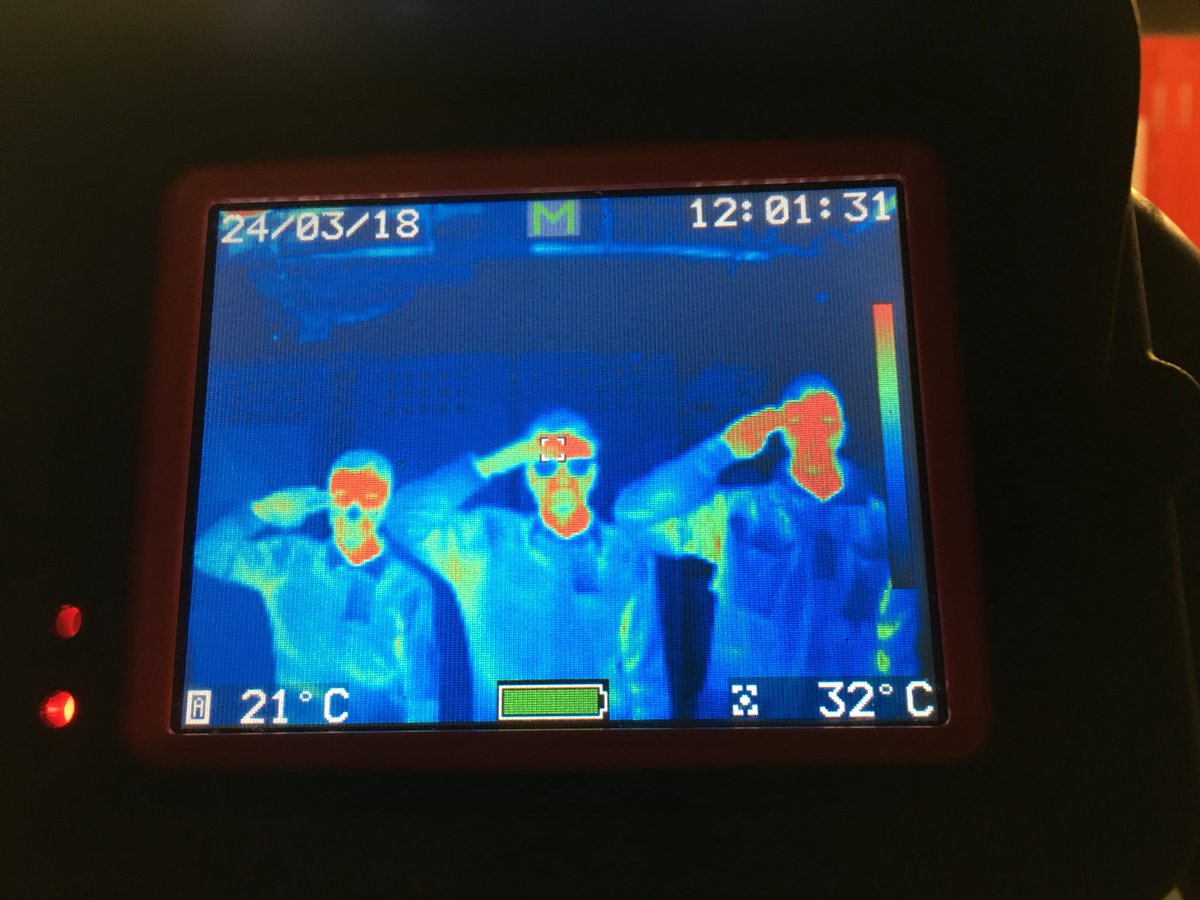 The screen of a thermal imaging camera showing three teenagers saluting