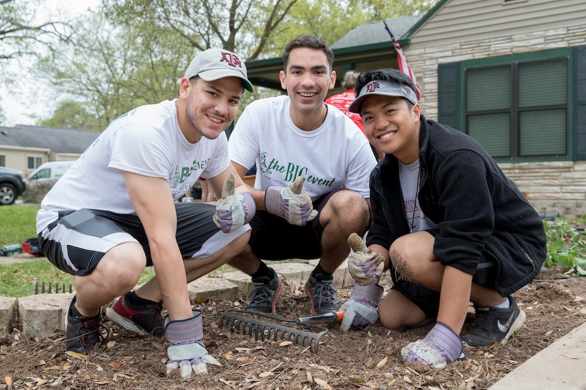 Three Aggies kneeling in mulch gigging 'em