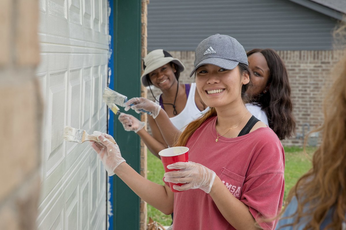 Three Aggies smiling for the camera while painting a garage door white