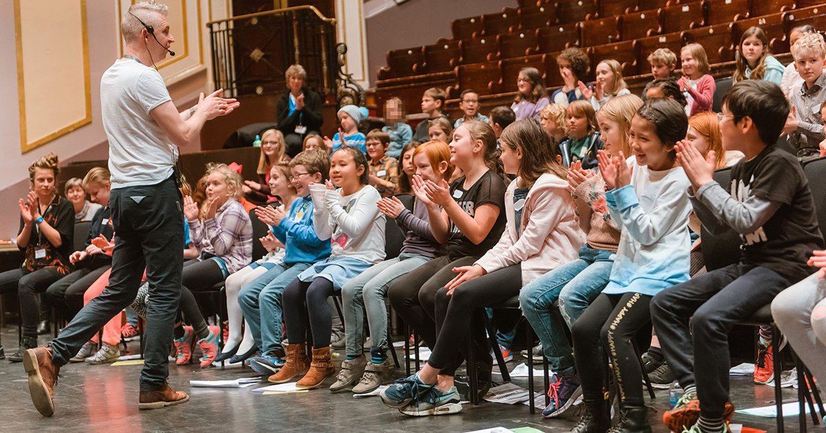 Photo of Love Music Junior Choir - children singing and clapping on Usher Hall stage, with conductor clapping.
