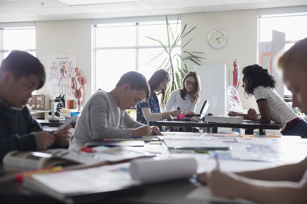 students crowding around and working at two desks in a grad school classroom