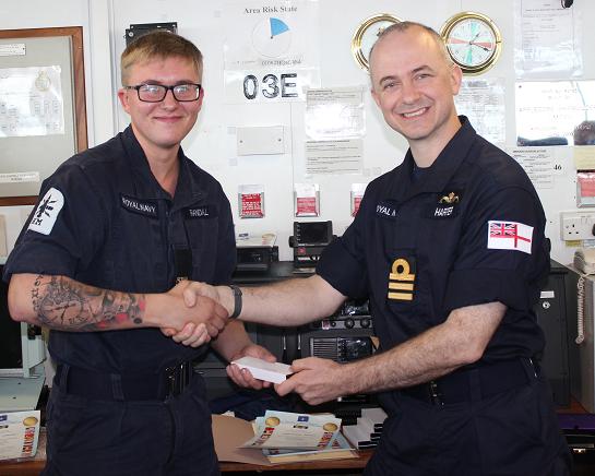 The same young sailor being awarded a prize by the commanding officer.