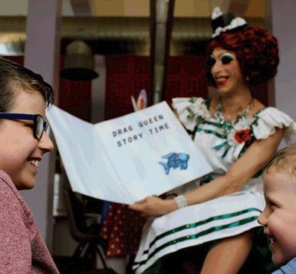 Drag queen reads story to two smiling children 