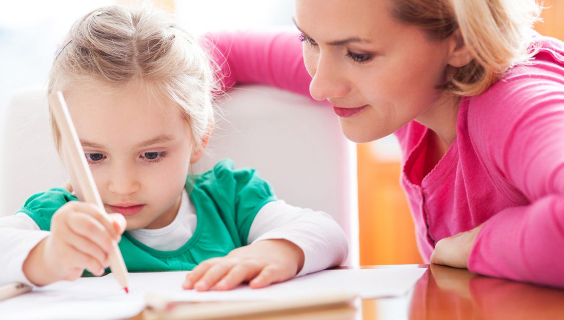 a mother watching her young daughter draw with a red marker from over her shoulder