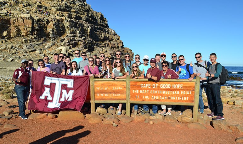 A group of Aggies standing at the Cape of Good Hope sign in South Africa with a Texas A&M flag