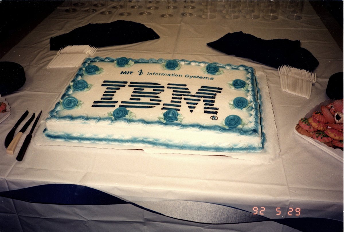 Picture of a sheet cake on a table with “MIT Information Systems” writing in icing at the top and a large IBM logo in Icing in the middle.