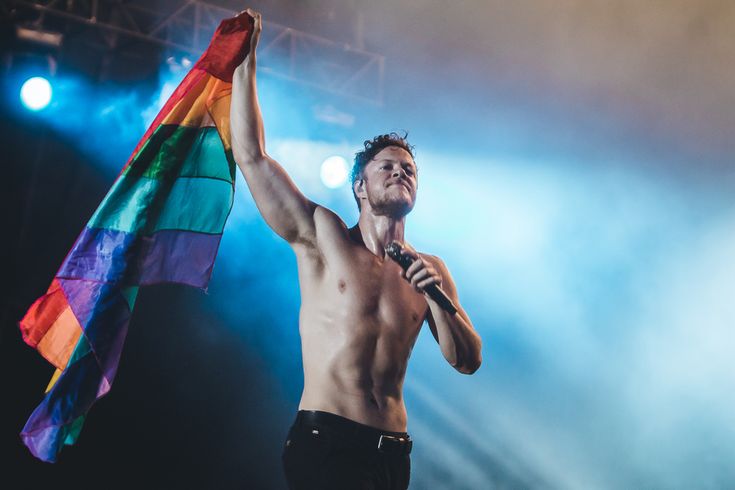 Happy birthday to a shirtless Dan Reynolds holding a pride flag 
