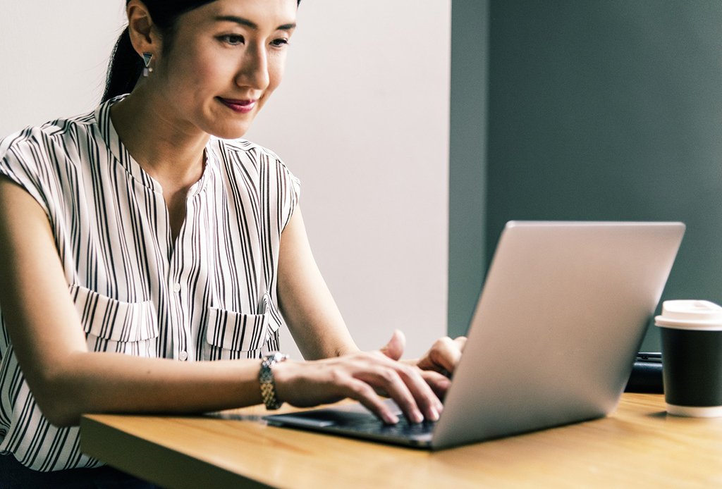 a woman sitting at a table smiling down at her taptop as she types 