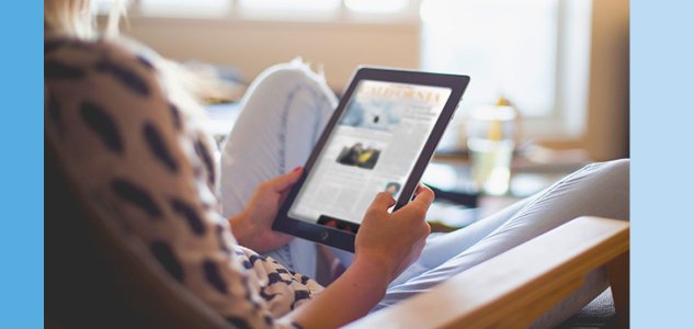 a woman sitting on her couch reading digital newspapers on her tablet