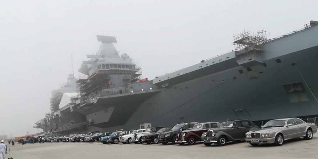The jetty in front of HMS Queen Elizabeth, filled with a wide range of old Rolls Royce and Bentley cars.