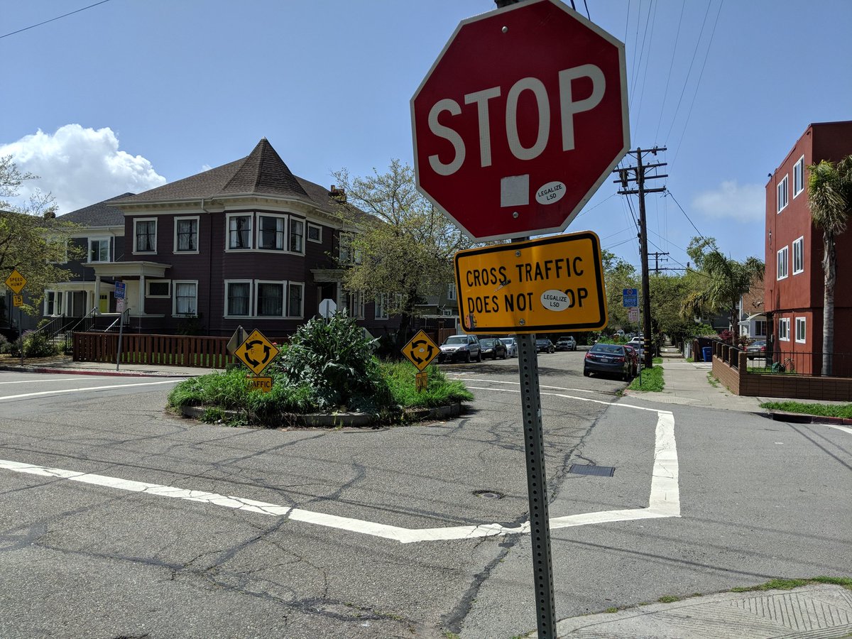 Roundabout with a stop sign and a sign underneath saying "Cross traffic does not stop", also with stickers encouraging LSD use