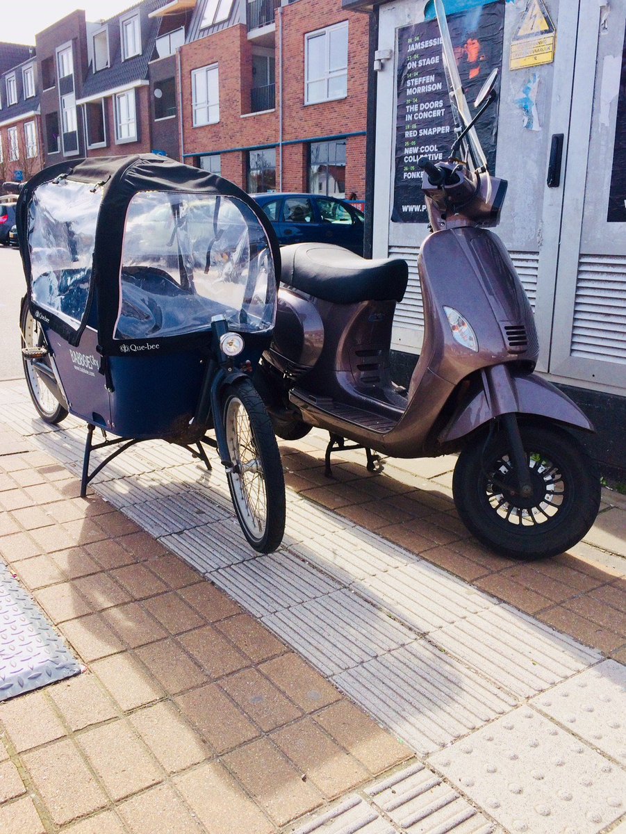 Een bakfiets en een scooter staan op de geleidelijn geparkeerd