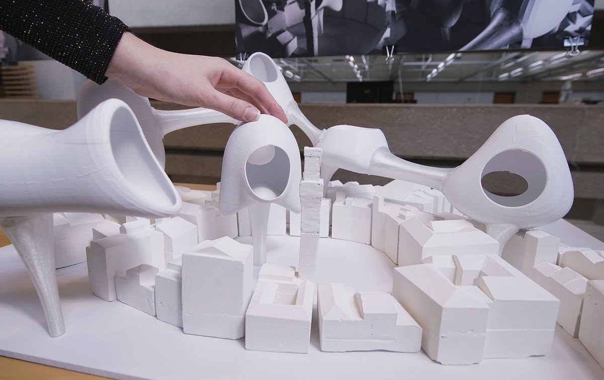 students hand resting on a white fabrication of modern looking, circular-shaped buildings resting on square cubes