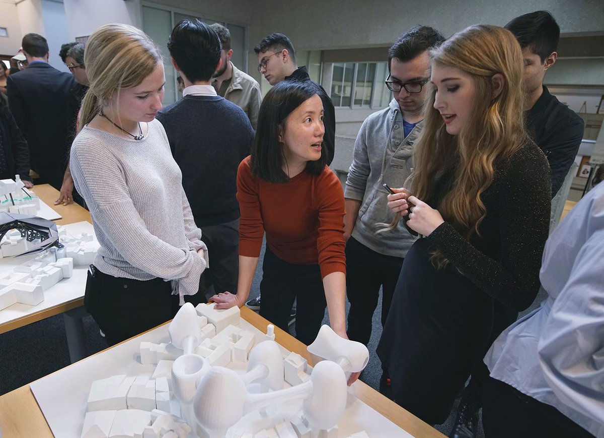 professor pointing to designs and talking to students around a model