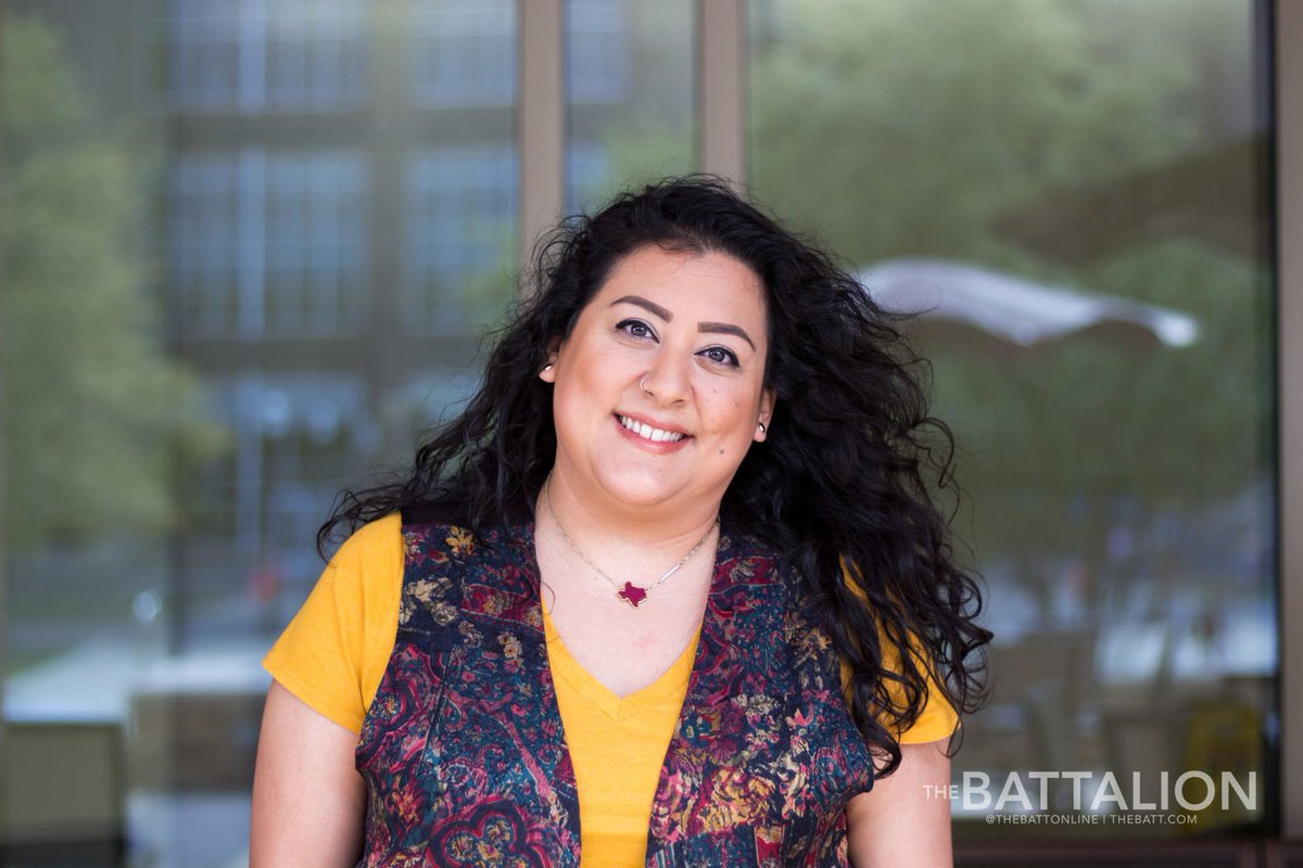 A happy student standing in front of the MSC wearing a yellow shirt, floral vest, and a Texas-shaped necklace