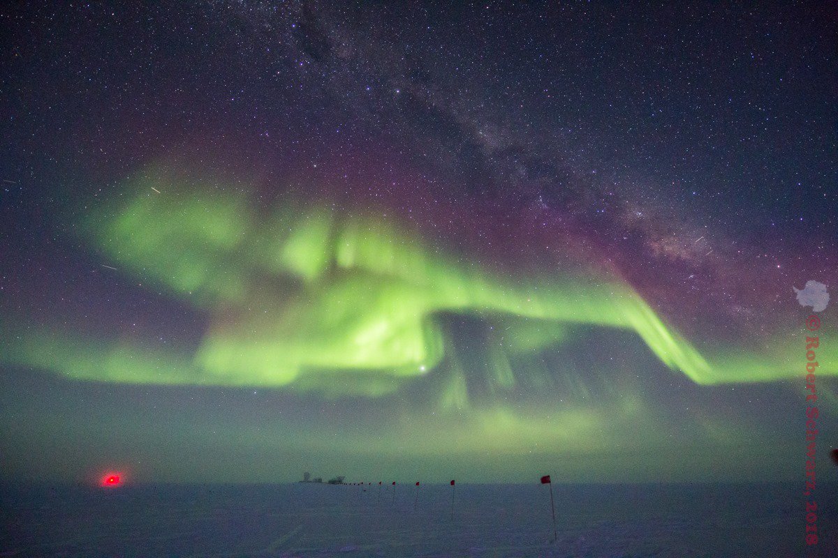 AntarcticReport's tweet photo. Aurora australis intensifies at South Pole; at top, Southern Cross &amp; pointers, Alpha and Beta Centauri. View towards the dark sector: silhouette of South Pole Observatory at center, red light at left, IceCube Neutrino Observatory @NSF @SPTelescope @uw_icecube pic @iceman_90South https://t.co/Z7Cv7pDUy1