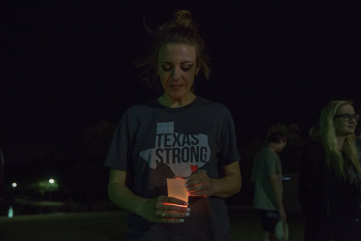 a lone woman standing and looking down at her candle in darkness