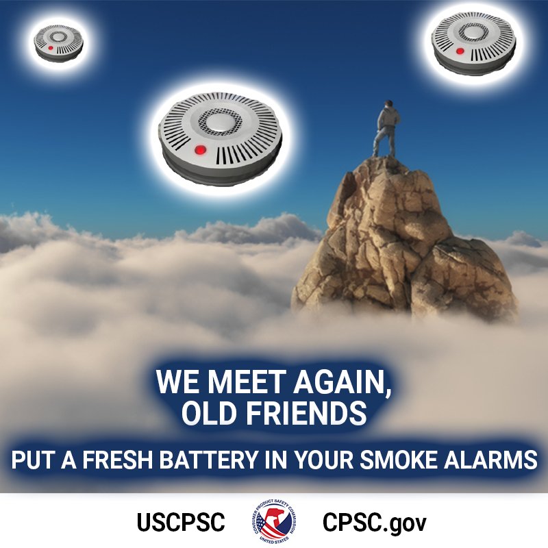 A person is standing on top of a mountain above the clouds. Three glowing spaceship smoke alarms hover over them. The text reads, "We meet again, old friends. Put a fresh battery in your smoke alarms."