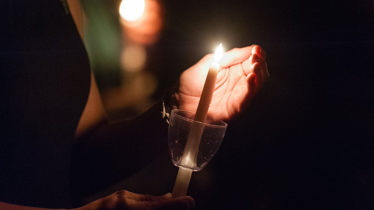 person holding a lit candle and shielding it with their left hand in darkness
