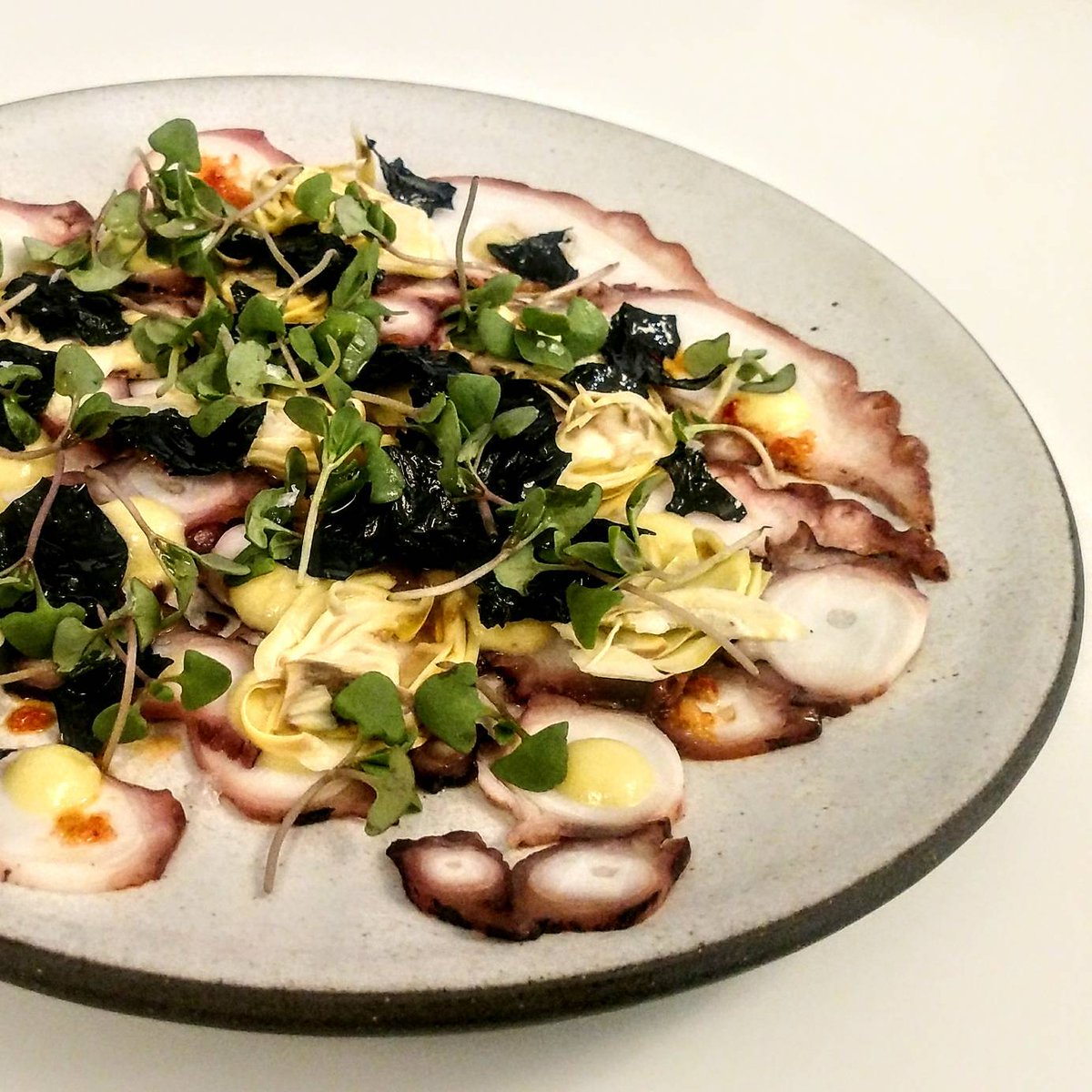 It's back!!! So excited to be bringing back one of our favorite warm weather dishes! Octopus carpaccio with shaved artichokes, Calabrian chile oil, lemon, &amp; squid ink chips!