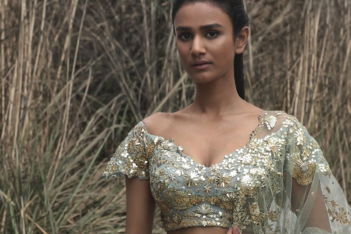 A pale ice-blue tulle and silk lehenga with delicate floral motifs and elongated Tree of Life spires rendered in hand crafted zardozi using kasab, gotta and beaten metal sequins, paired with an off-shoulder blouse and tulle dupatta