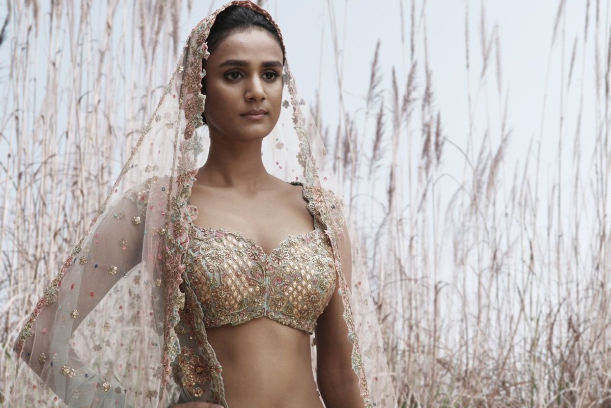 An ice-blue silk and tulle lehenga featuring motifs inspired by Rajasthani Haveli windows and jharokhas, and florals derived from vintage textiles.  The lehenga is paired with a gotta and zardozi choli and sheer odhnis in ice-blue and ashes of rose.