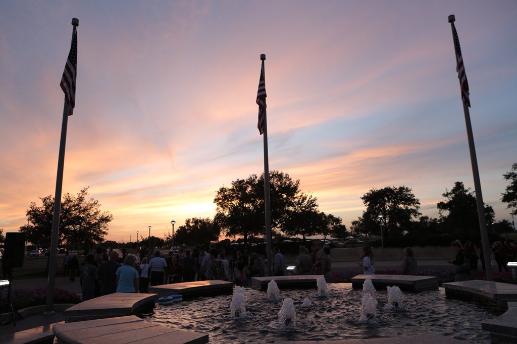 Sun setting with US flags on flag poles around a fountain