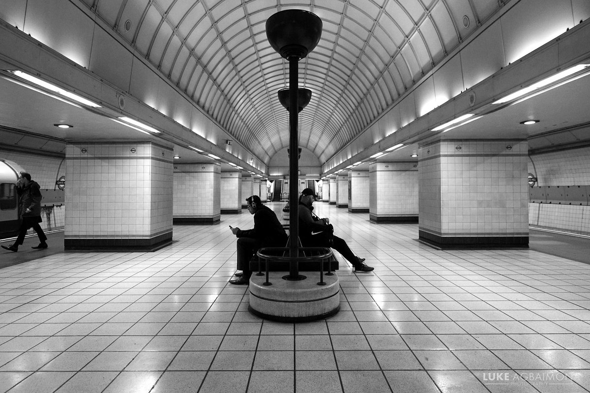 Commuters wait at #GantsHill underground station by Luke Agbaimoni ☺

More #London #photography
tubemapper.com/gants-hill-sta…

#travel #streetphotography #blackandwhite #architecture #symmetry #tfl