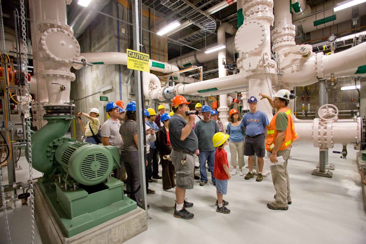 A group of people are touring inside the Brightwater treatment plant, surrounded by large pumps, pipes and equipment. It is clean and smells good because all the smelly processes are covered!!!