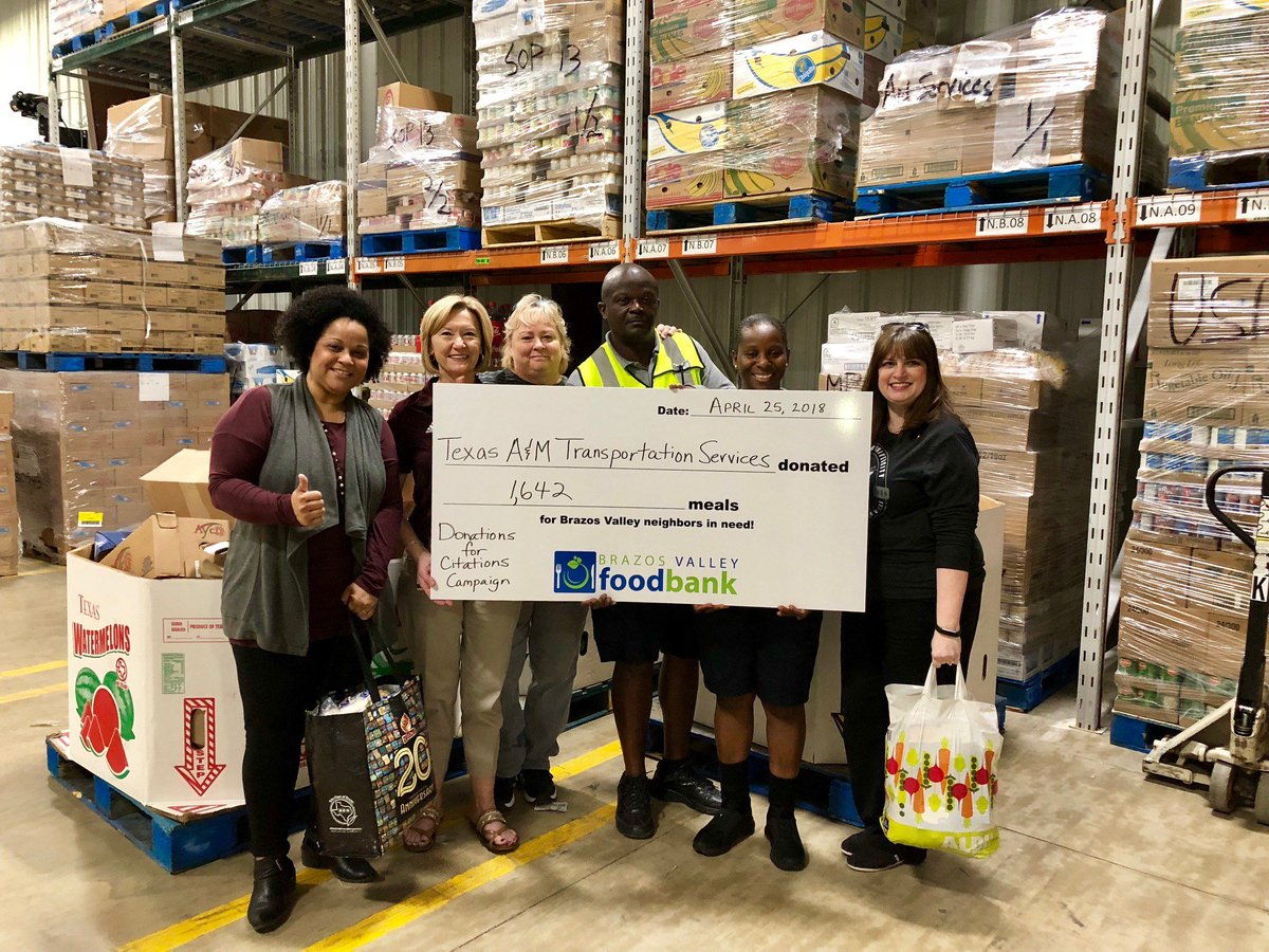 representative from transportation services and the food bank holding a large check in front of donated produce in warehouse