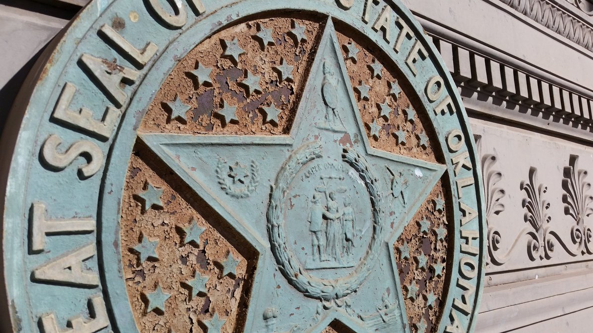 OKStateCapitol's tweet image. Before and after pictures of the cast iron state seal above the historic main entrance. Paint analysis by @EverGreeneAA determined the original colors on the seal.