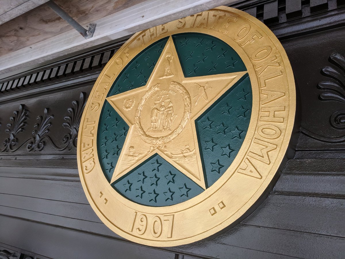 OKStateCapitol's tweet image. Before and after pictures of the cast iron state seal above the historic main entrance. Paint analysis by @EverGreeneAA determined the original colors on the seal.