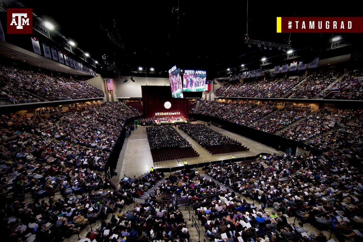 View of a full Reed Arena from the upper concourse during a graduation with students seated in chairs on the floor facing the stage