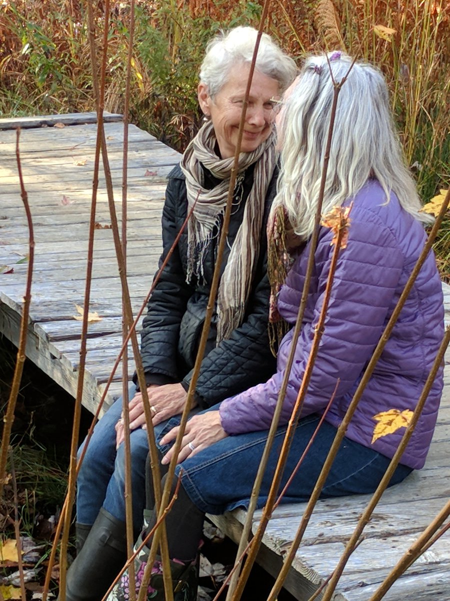 Rosmarie sits with one of her mentors Margret Drescher from Windhorse Farm. They sit side by side on a small wooden bridge as they smile at one another and catch up.