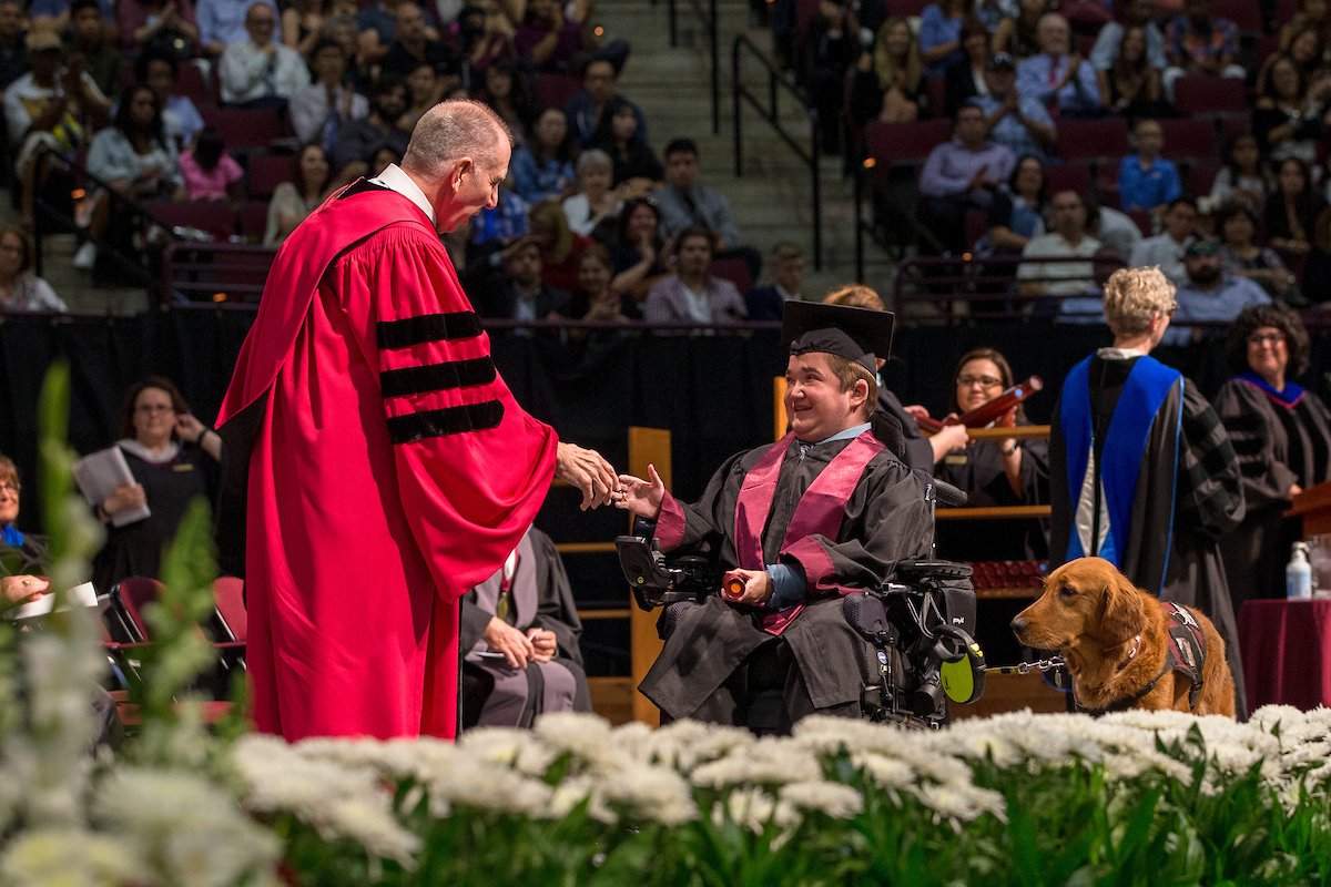 student in wheelchair shaking president Young's hand on stage with service dog at his side