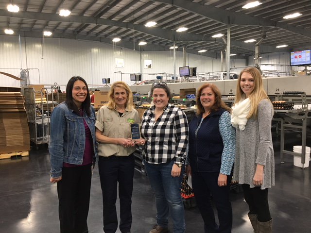 Staff from Kreider Farms, OVR and the Next Step Program smile for a photo inside Kreider Farms’ warehouse. Kreider Farms staff are holding their employer award in the photo.