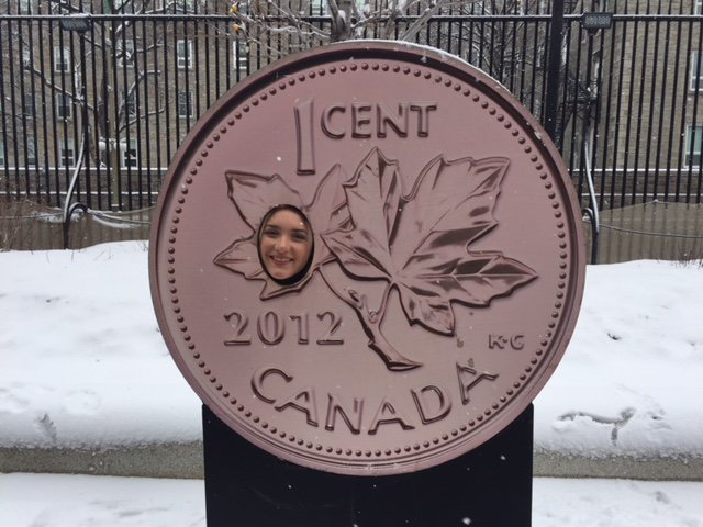 Shelby Travers smiles with her face inside a giant, novelty penny with maple leaves and the year 2012 written on it.