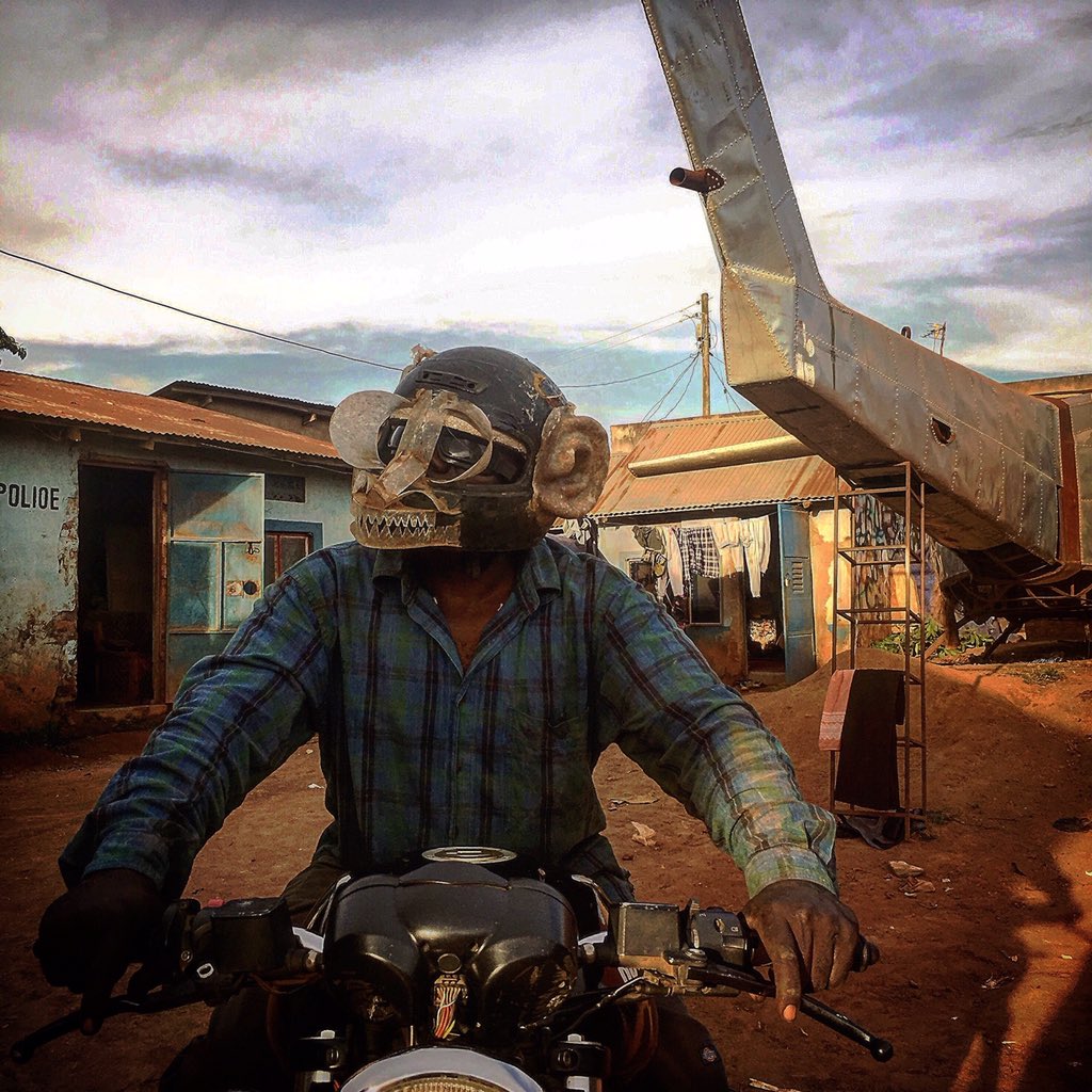 IPAUganda's tweet photo. An actor with independent cinema studio #Wakaliwood, mounting a motorbike while wearing a monkey mask in #Kampala, with the helicopter he is building in the background, in this #postcard by FCAU’s @fuddish #documentaryphotography #everydayuganda https://t.co/RHGRozbYyW