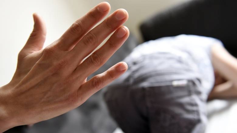 A close-up photograph of an adult's hand, looking as though it is about to spank a child.