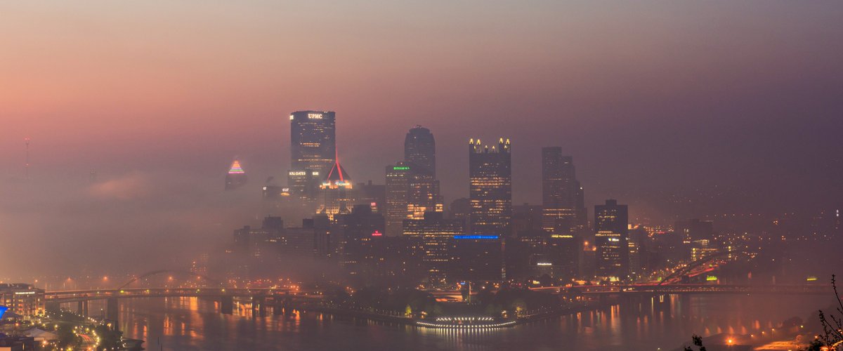 DaveDiCello's tweet photo. A pink, hazy sky backdrops downtown #Pittsburgh as fog creeps into the city from the rivers, creating a surreal yet beautiful scene just before sunrise on a spring morning. https://t.co/fmKqlQxHAg