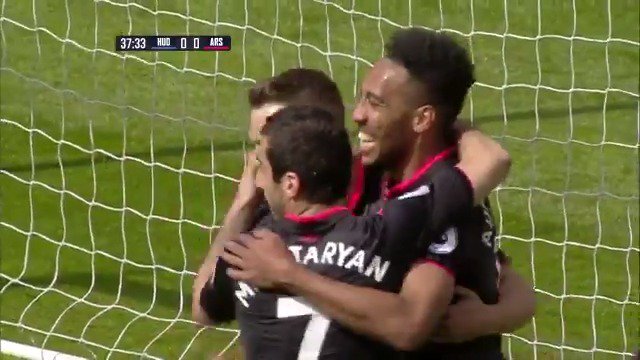 Soccer players in black jerseys celebrate a goal near the net, with one player's jersey reading 'TARYAN'. The broadcast scoreboard shows '37:33 MUN 0 - 0 ARS'.
