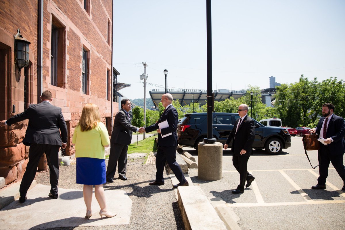 Image of Governor Tom Wolf being greeted at the entrance to a building on a sunny day.