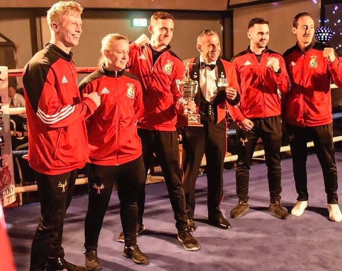 Five men and one woman from the Boxing Squad, plus an official, pose in team kit and with their large shiny trophy!