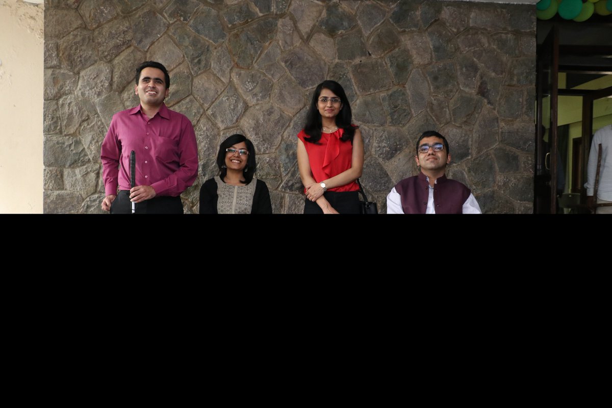 4 panelists are seen standing against a stone wall. From left to right are Rahul Bajaj wearing a lavender shirt and black trousers and holding a cane in front of him, Pratishtha Deveshwar sitting on a wheelchair wearing back and beige, Saumya Sharma dressed in a red sleeveless shirt and black trousers and Nipun Malhotra dressed in a white shirt, dark pants and a brown sleeveless jacket on his wheelchair.