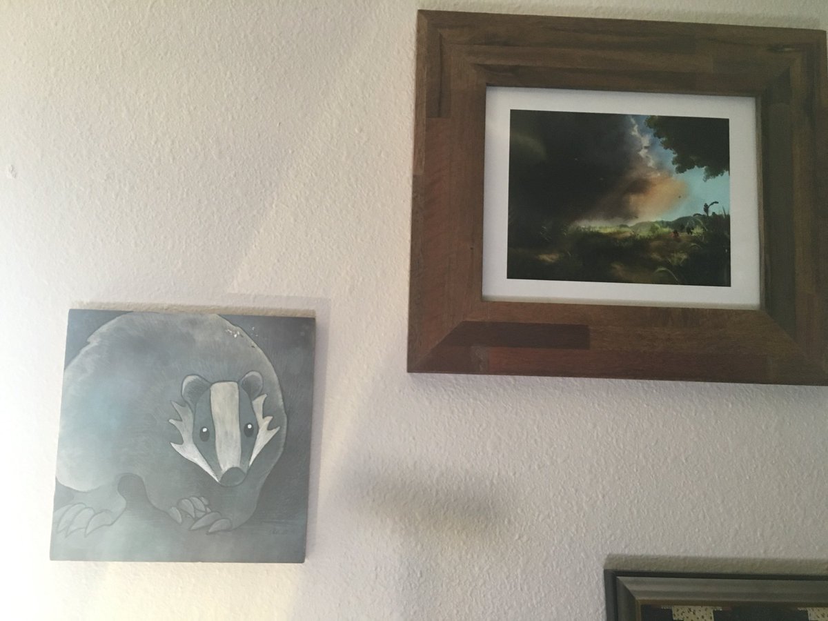 Photo of two paintings: a square badger and a stormy landscape.