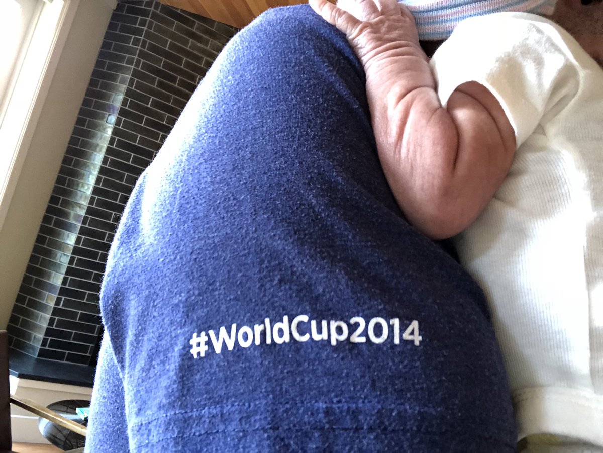 A baby is draped across the shoulder of a dad. Printed, in white, on the blue shirtsleeve of the dad, is the hashtag"#WorldCup2014".